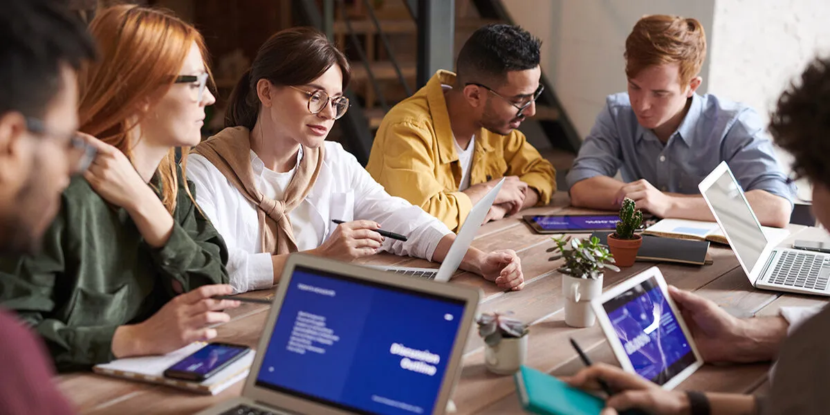 A team leaning over a wooden table, working together on laptops